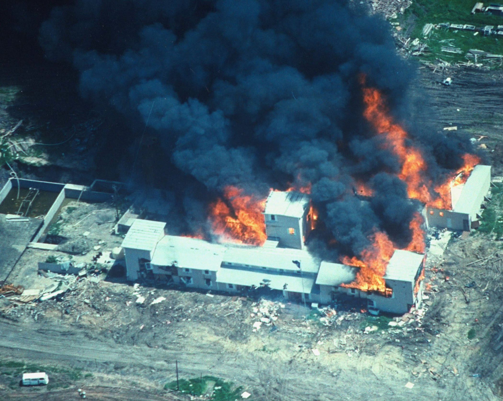 Overhead of smoking fire consuming David Koresh-led Branch Davidian cult compound, believed set by cult after FBIATF teargassing in effort to end siege
